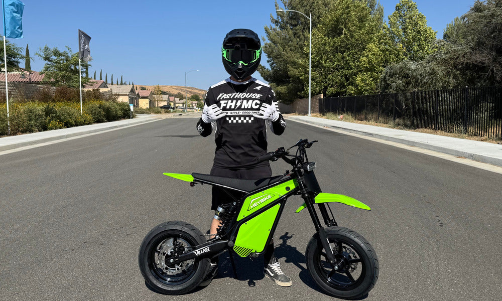 Rider standing behind a green Heybike electric dirt bike on a paved road.